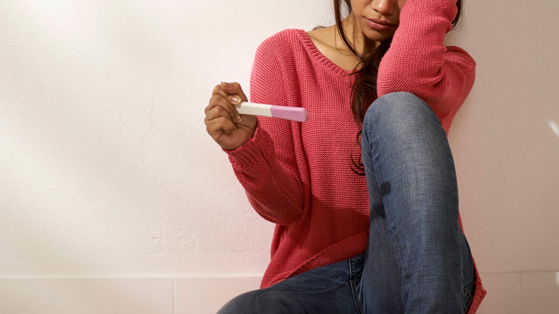 Eine junge Frau hält einen Schwangerschaftstest in der Hand.