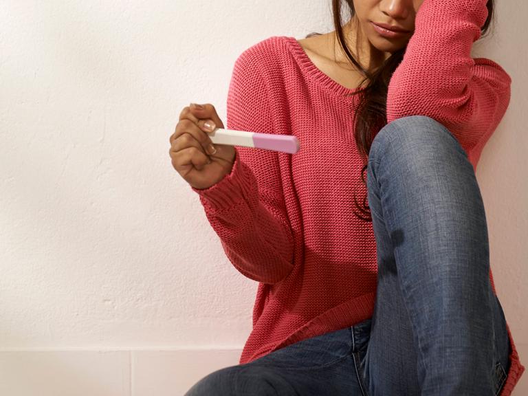 Eine junge Frau hält einen Schwangerschaftstest in der Hand.
