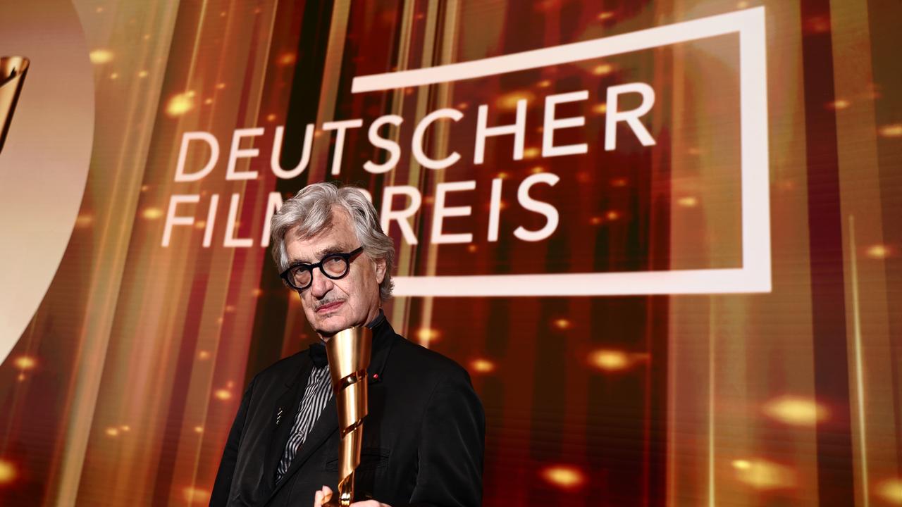 Wim Wender hält auf der Bühne den Ehrenpreis des Deutschen Filmpreises in der Hand. Hinter ihm steht in großer weißer Schrift "Deutscher Filmpreis".