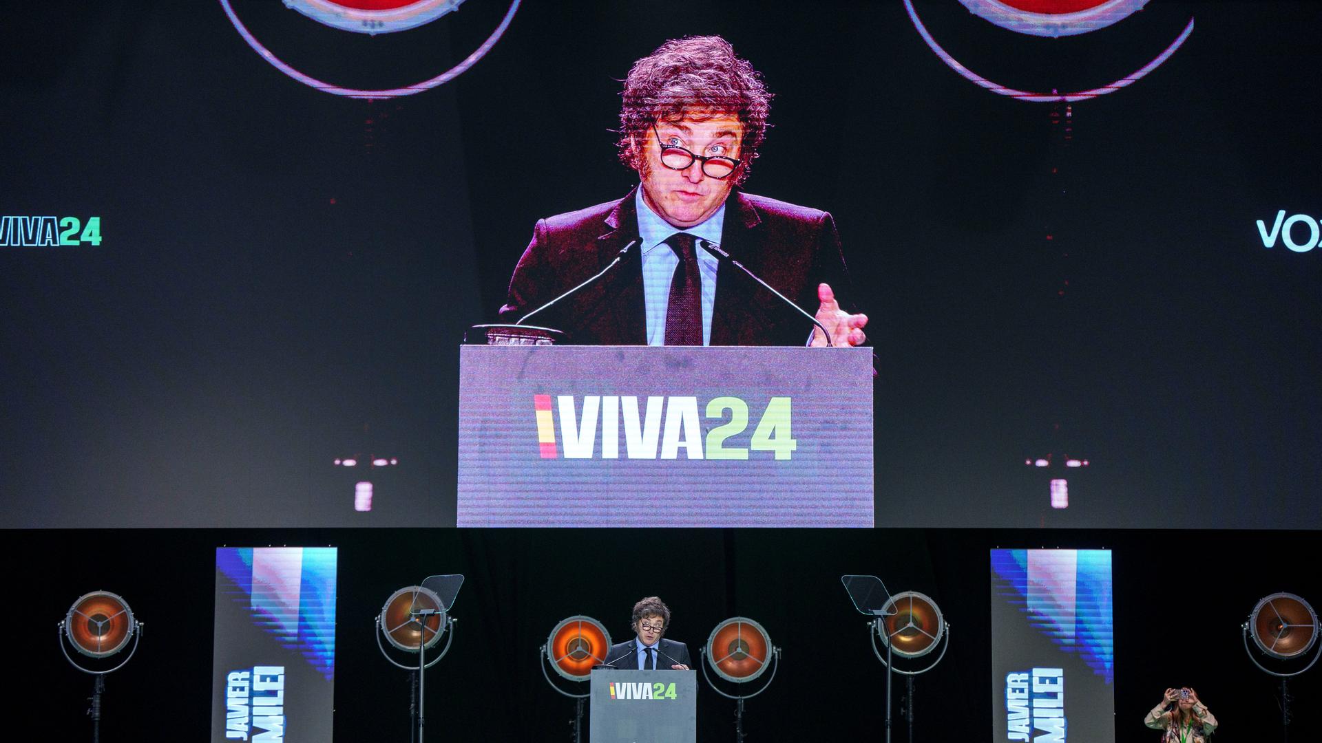 Argentiniens Präsident Javier Milei steht auf einer Bühne hinter einem Rednerpult mit der Aufschrift "Viva24". Sein Bild wird dahinter auf eine riesige Video-Leinwand übertragen. 
