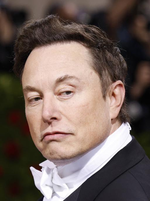 Elon Musk im schwarzen Anzug mit weißer Fliege schaut nach links über die Schulter.