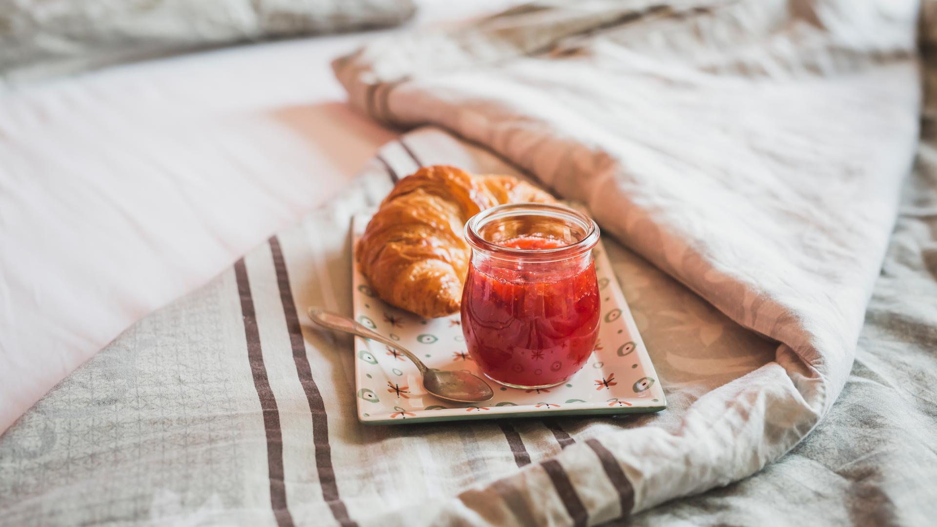 Ein Teller mit einem Croissant und Erdbeermarmelade steht auf einem Bett.