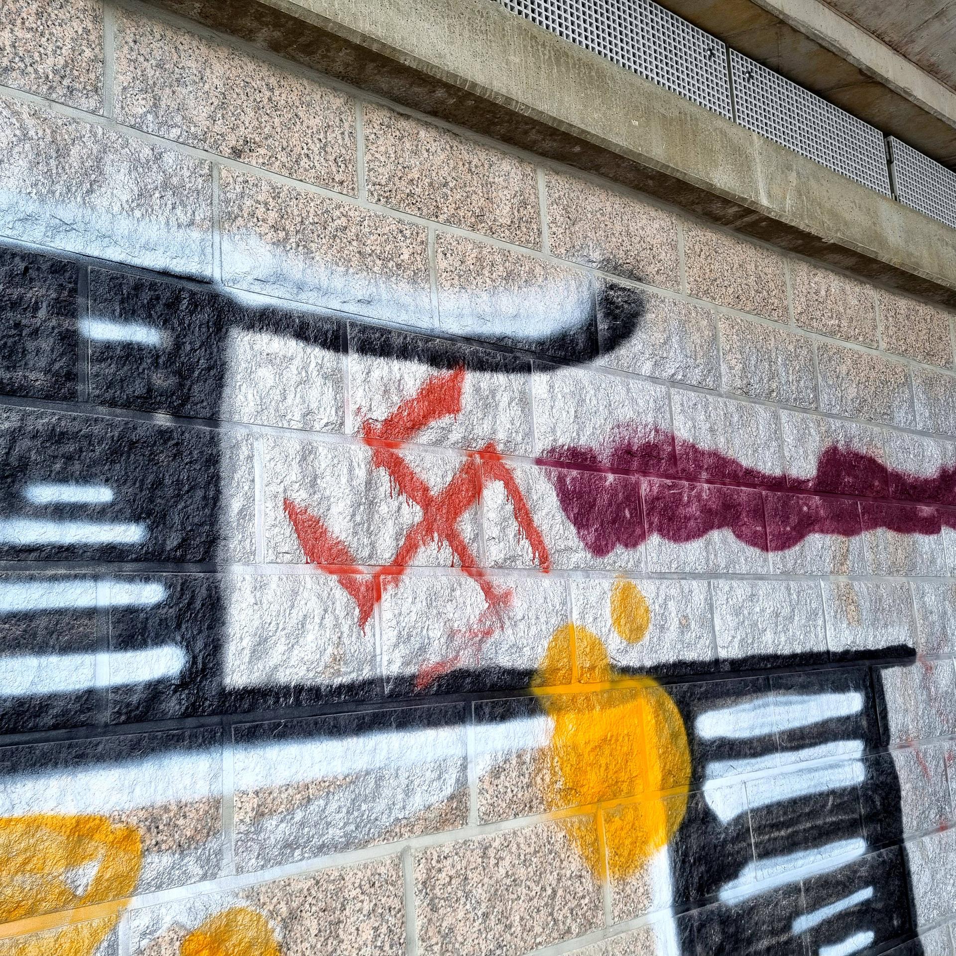 Rote Hakenkreuz-Schmiererei an einer mit Graffitis besprühten Wand.