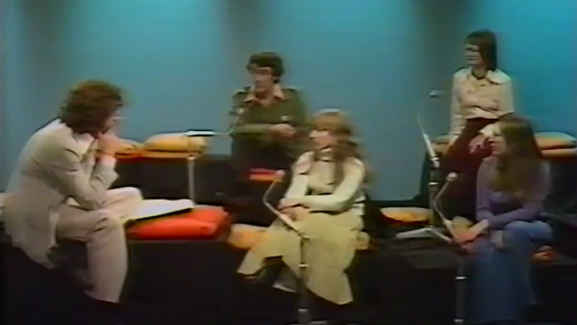 Das Foto zeigt eine Szene aus einer alten britischen Talksendung im Fernsehen. Ein Gruppe von Menschen hockt in einer Sitzgruppe. Einige Personen reden, die anderen hören zu.
