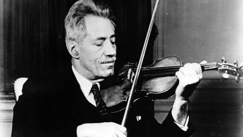 Die Schwarzweiß-Fotografie von ungefähr 1935 zeigt Fritz Kreisler in Anzug und Krawatte beim Spielen seiner Violine.