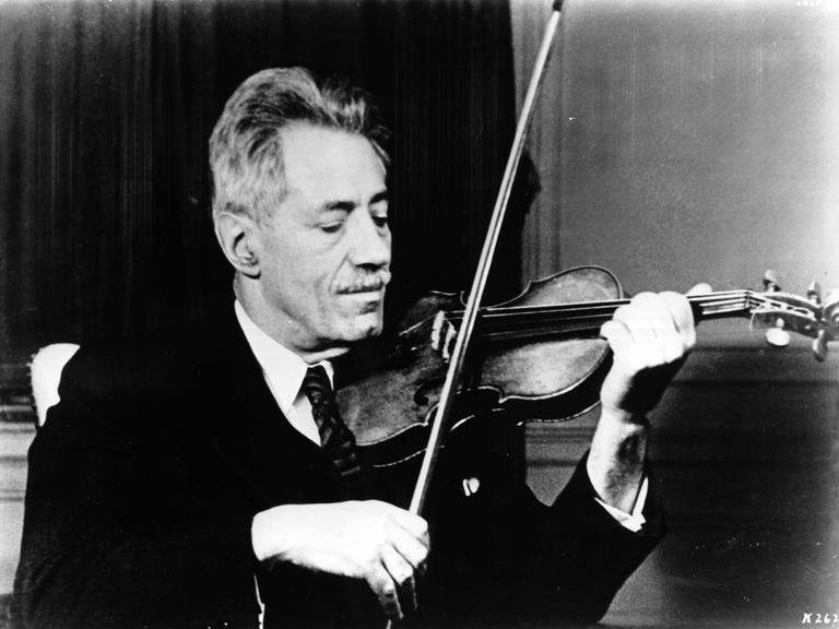 Die Schwarzweiß-Fotografie von ungefähr 1935 zeigt Fritz Kreisler in Anzug und Krawatte beim Spielen seiner Violine.