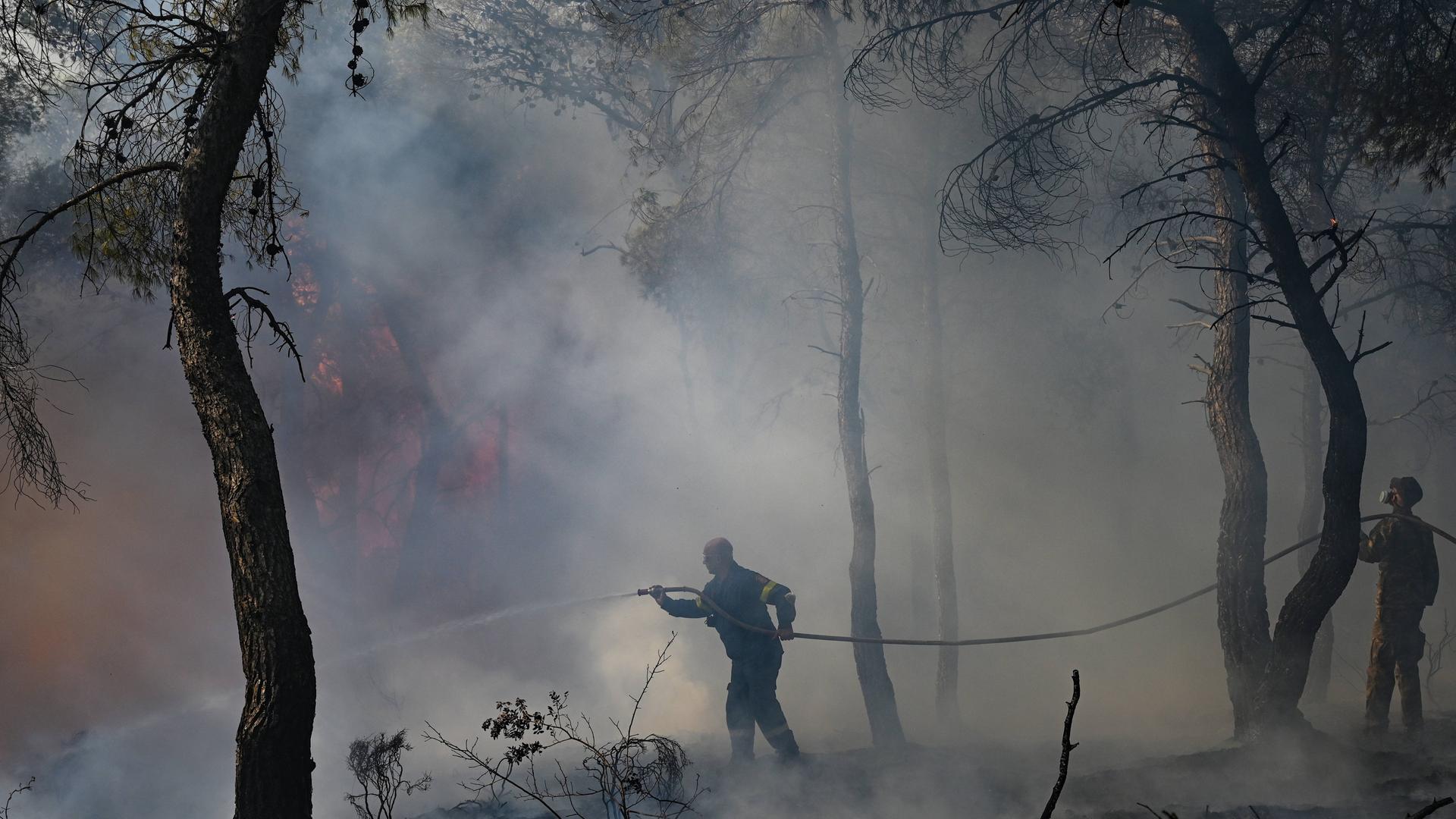 In Griechenland löschen zwei Feuerwehrmänner einen Waldbrand; um sie herum ist Rauch und Feuer zu sehen. 24.08.2023