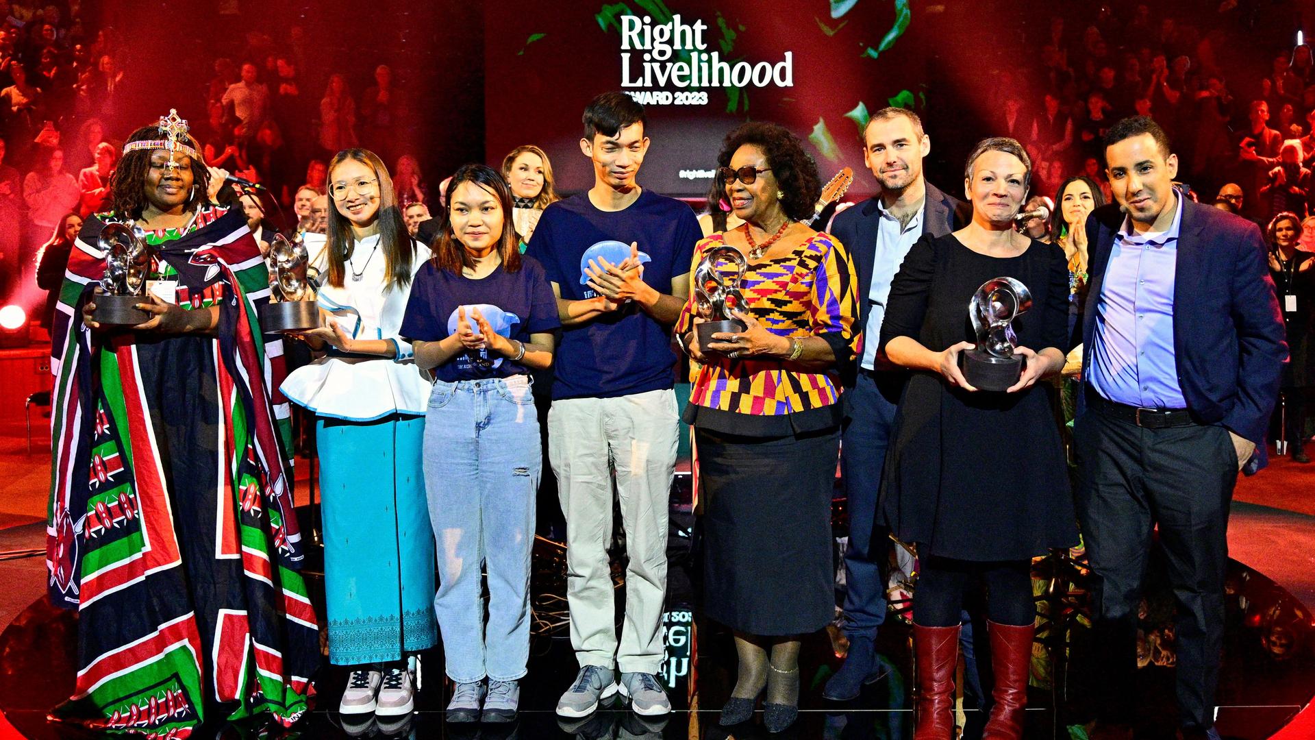 Eine Gruppe von Männern und Frauen, eine davon in afrikanischem Gewand, steht auf einer Bühne mit der Aufschrift "Right Livelihood Award 2023". Sie halten ihre Auszeichnungen in den Händen.