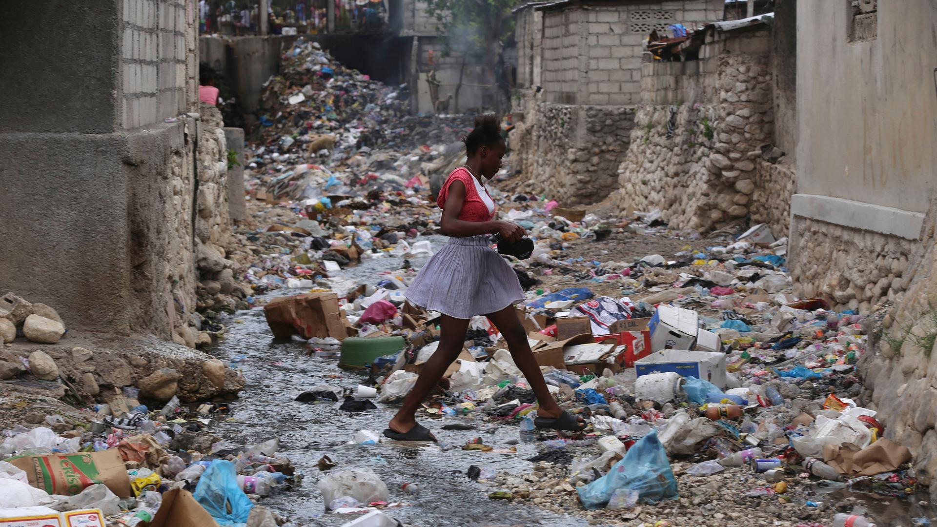 Ein Mädchen geht in Port-au-Price über eine Straße, die komplett mit Müll bedeckt ist.