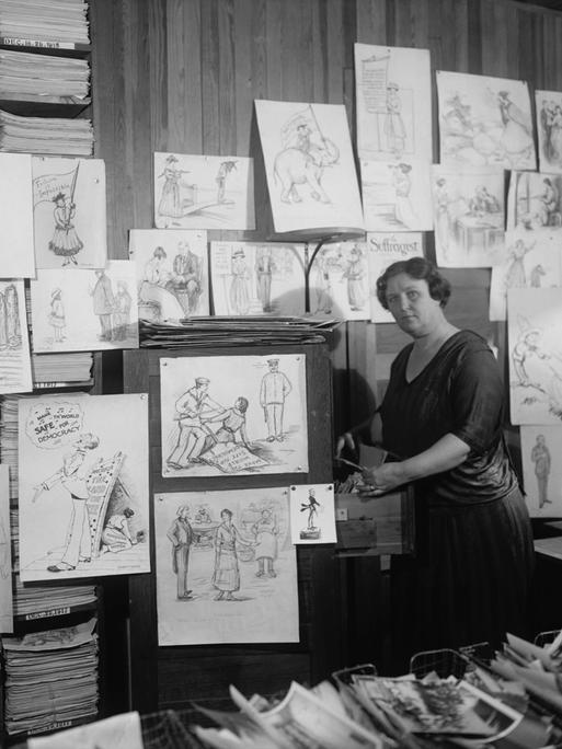 Frau auf Schwarz-Weiß-Foto steht in mitten von Zeichnungen in einer Zeitungsredaktion.