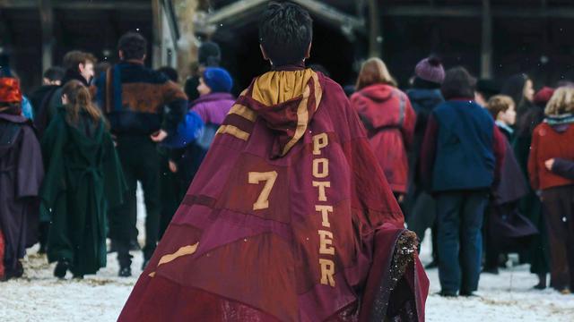 Eine Syene aus der neuen HBO Serie zu Harry Potter. Eine Person mit einem Umhang auf dem die Zahl 7 neben dem Namen Potter steht ist von hinten zu sehen, während sie auf eine Gruppe Personen zugeht.
