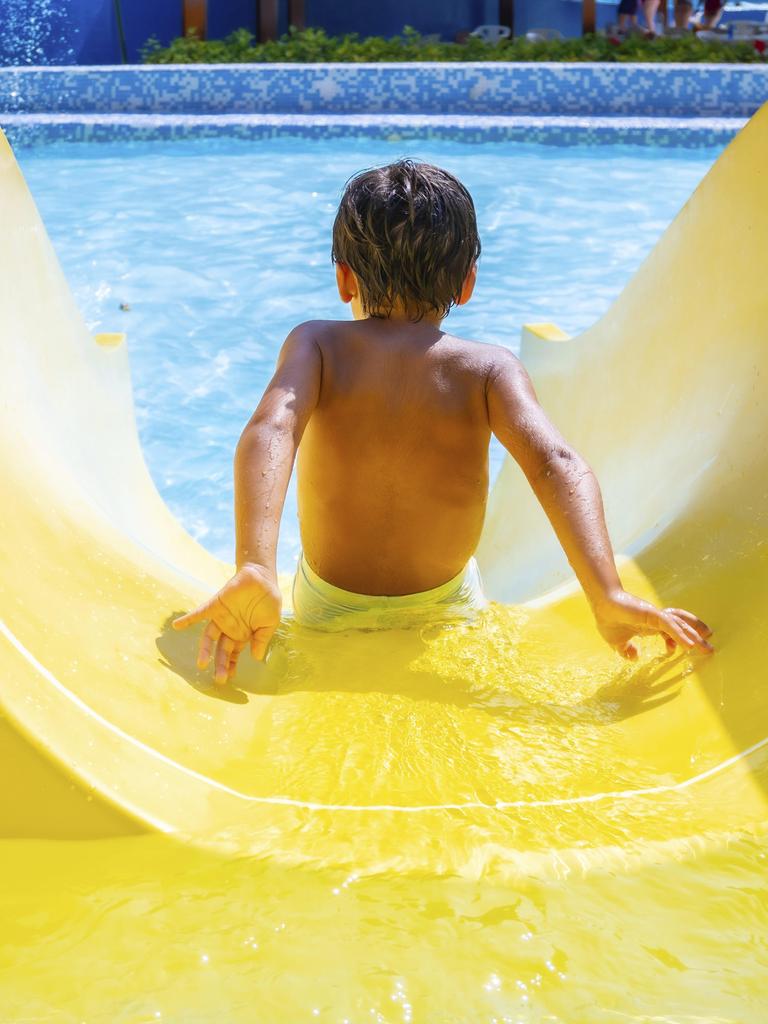 Ein Kind rutscht freudig eine gelbe Wasserrutsche in einem Freibad hinunter.