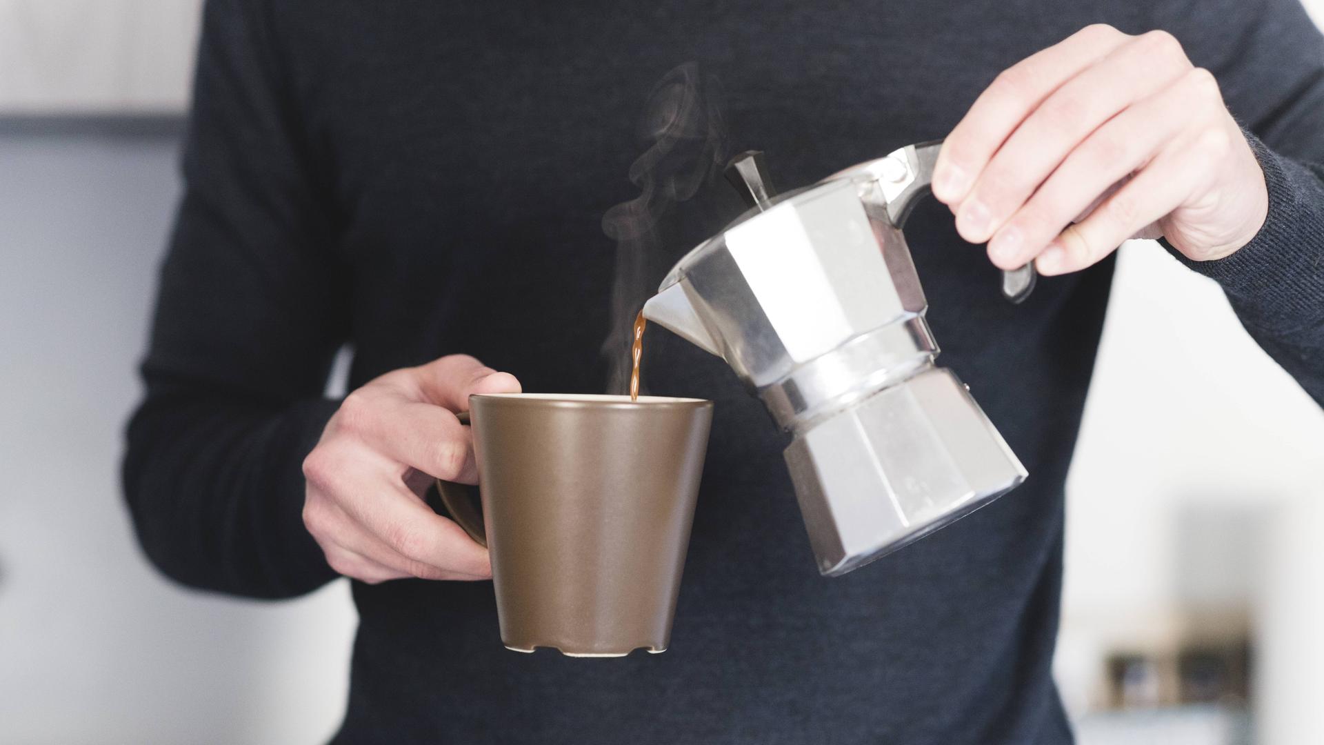 Ein Mann gießt heißen Espresso aus einer Kanne in einen Becher.