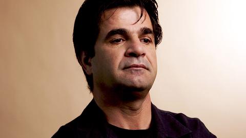 Porträt von Jafar Panahi mit verschränkten Armen und nachdenklichem Gesichtsausdruck.