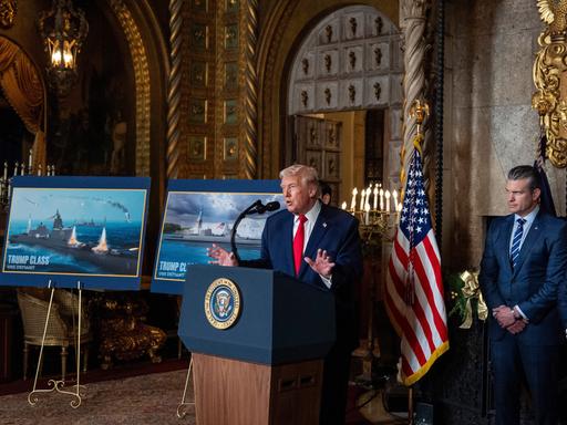 Donald Trump an einem Rednerpult, daneben Bilder von geplanten Schlachtschiffen, die nach ihm benannt werden sollen.