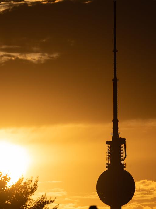 Blick auf den Berliner Fernsehturm an einem heißen Sommerband, im Hintergrund geht die Sonne unter. 