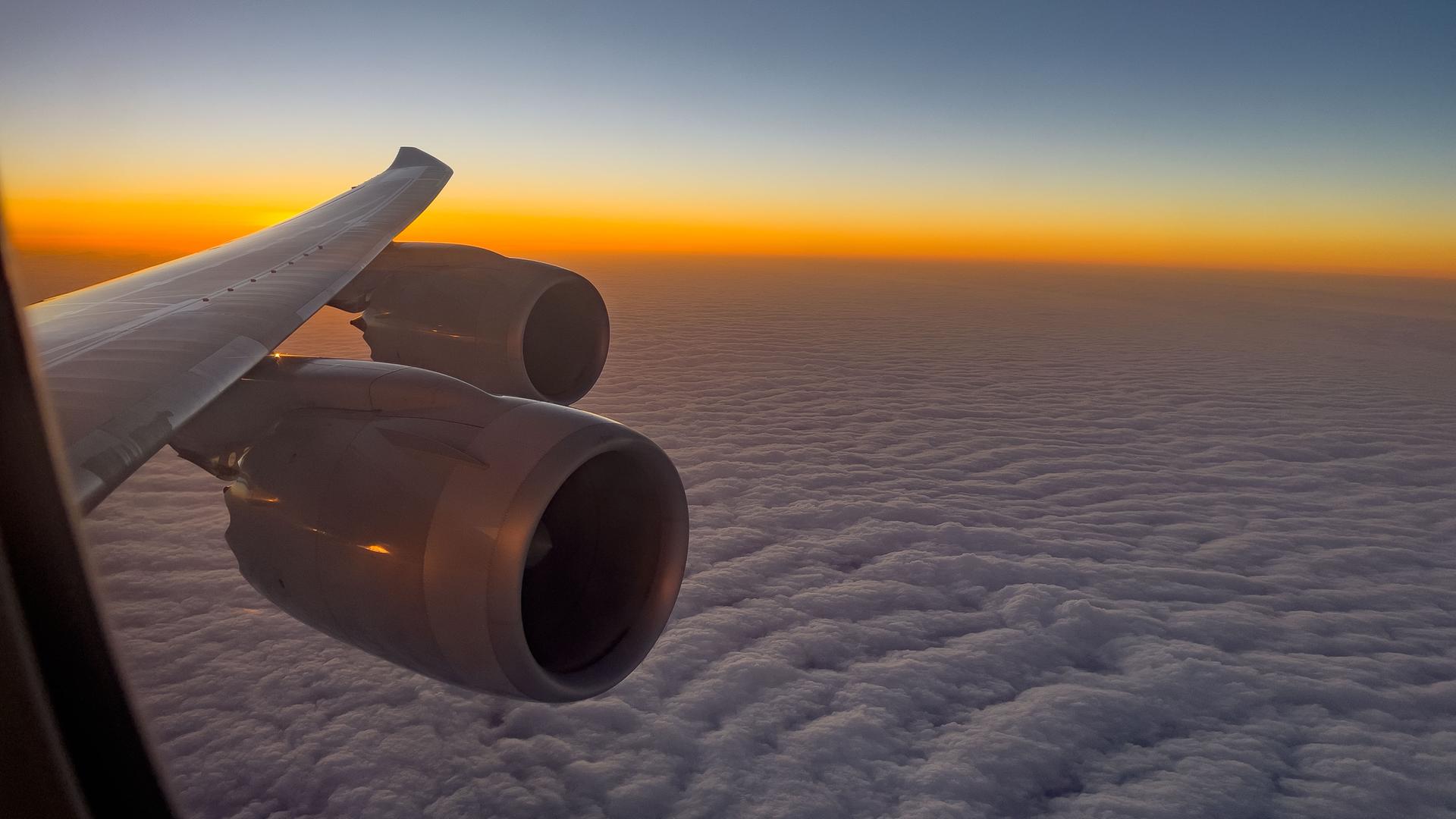 Blick aus einem Flugzeugfenster auf Wolken und einen Sonnenaufgang.