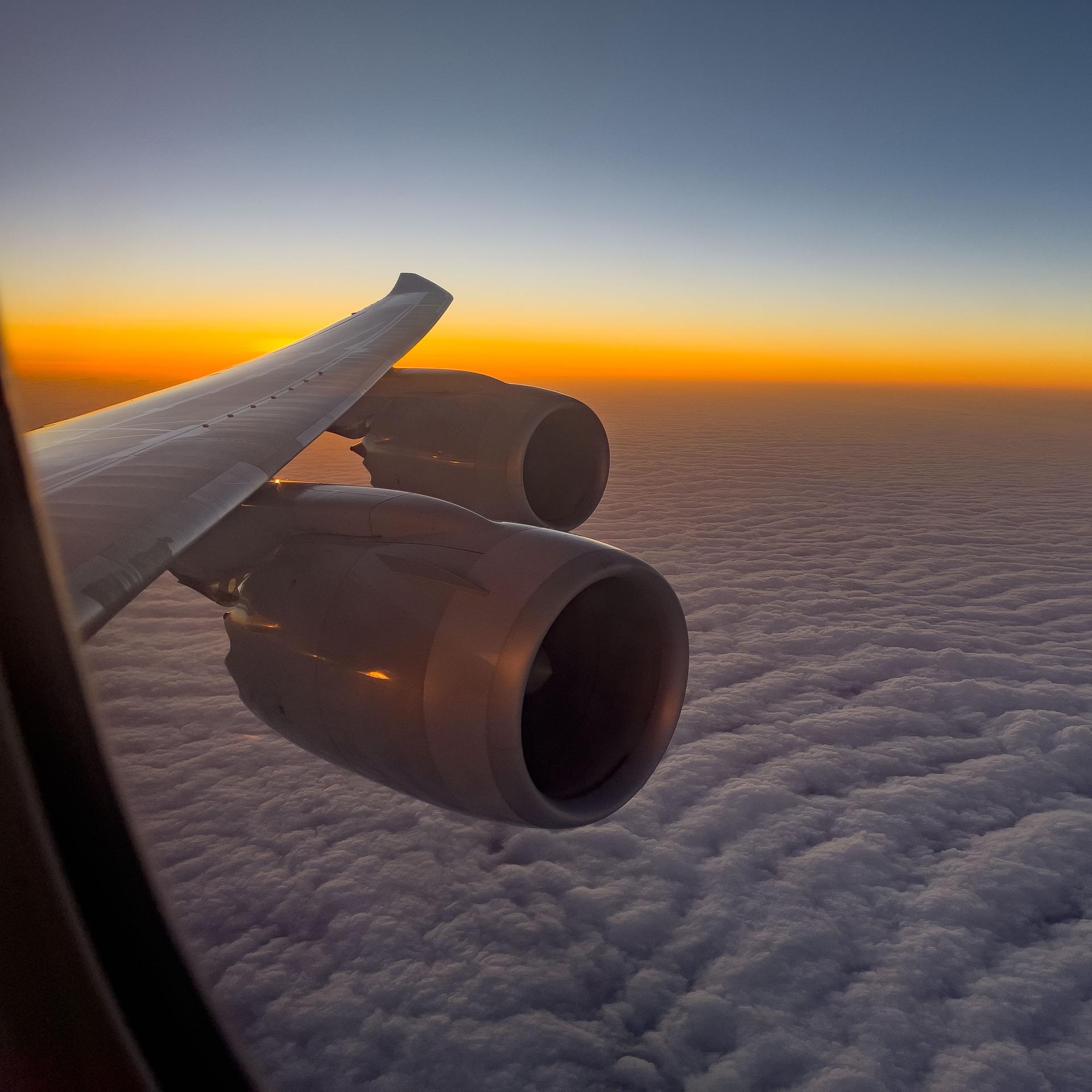 Blick aus einem Flugzeugfenster auf Wolken und einen Sonnenaufgang.