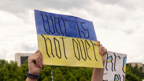 Eine Person hält vor dem Kanzleramt in Berlin ein Plakat mit der Aufschrift „War is not over“ in die Höhe. 