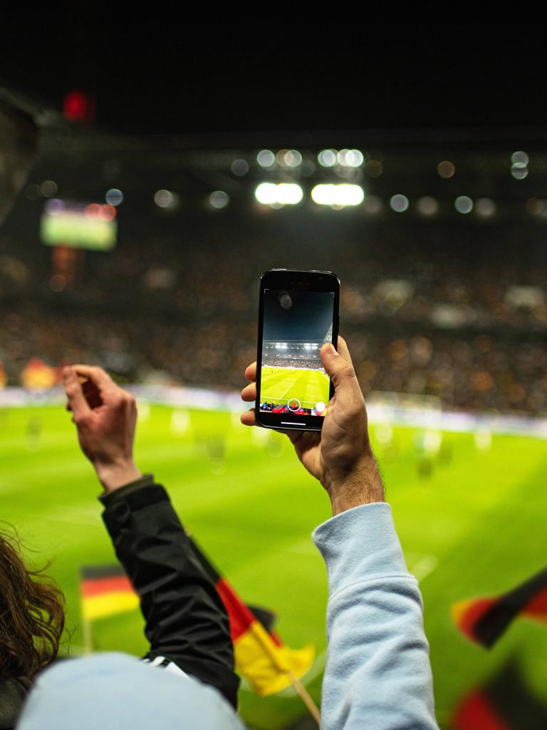 In einem Fußballstadion werden Deutschland-Flaggen geschwenk, jemand hält ein Smartphone in die Höhe