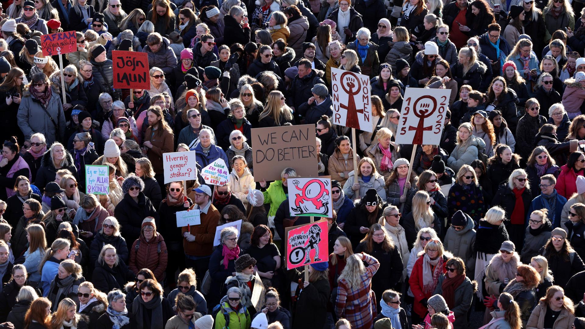 Eine protestierende Menschenmenge steht auf einem Platz. Ein Frau hält ein Schild mit der Aufschrift: "We can do better."
