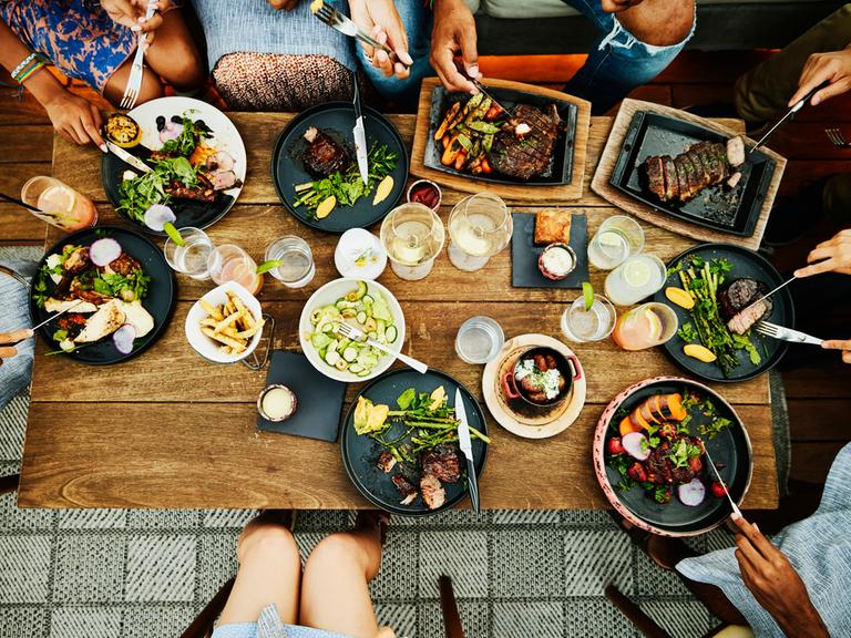 Mehrere Menschen sitzen um einen Essenstisch und speisen gemeinsam.