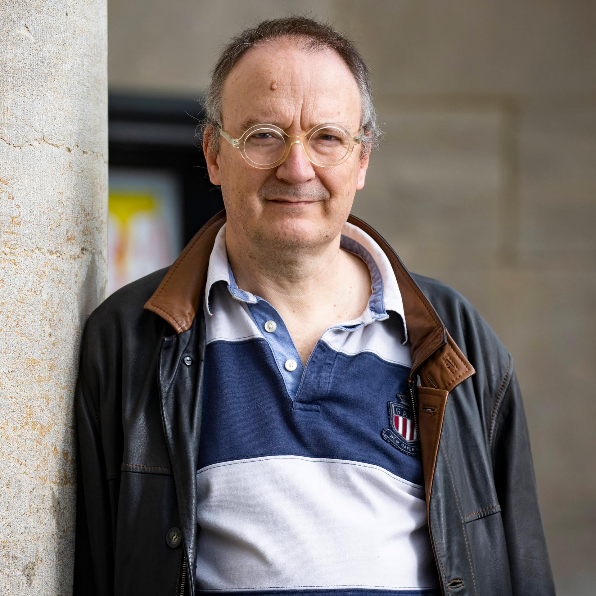 Thomas Brussig posiert in Polohemd und Nappalederjacke im Freien für ein Porträt.
