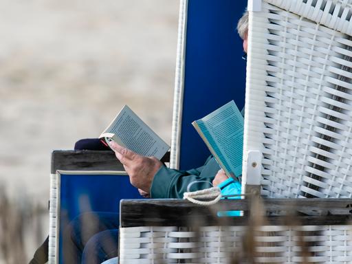 Zwei Personen sitzen bei stürmischem Wetter am Strand von Westerland im Strandkorb und lesen.