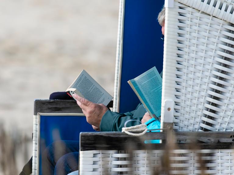 Zwei Personen sitzen bei stürmischem Wetter am Strand von Westerland im Strandkorb und lesen.