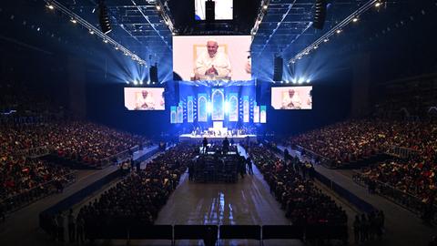 Papst Franziskus ist in einem Stadion auf einer großen Leinwand zu sehen