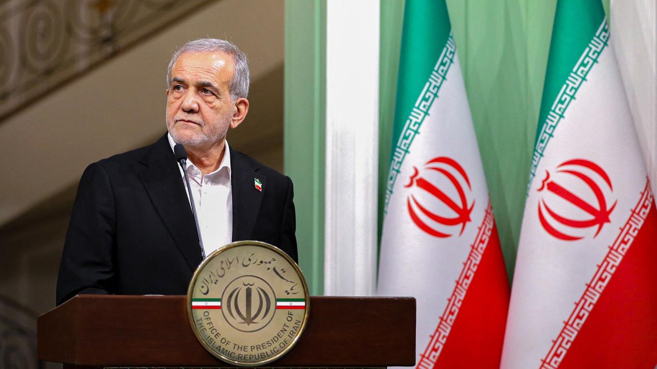 Massud Peseschkian steht an einem Redepult, im Hintergrund sind Staasflaggen des Iran zu sehen.