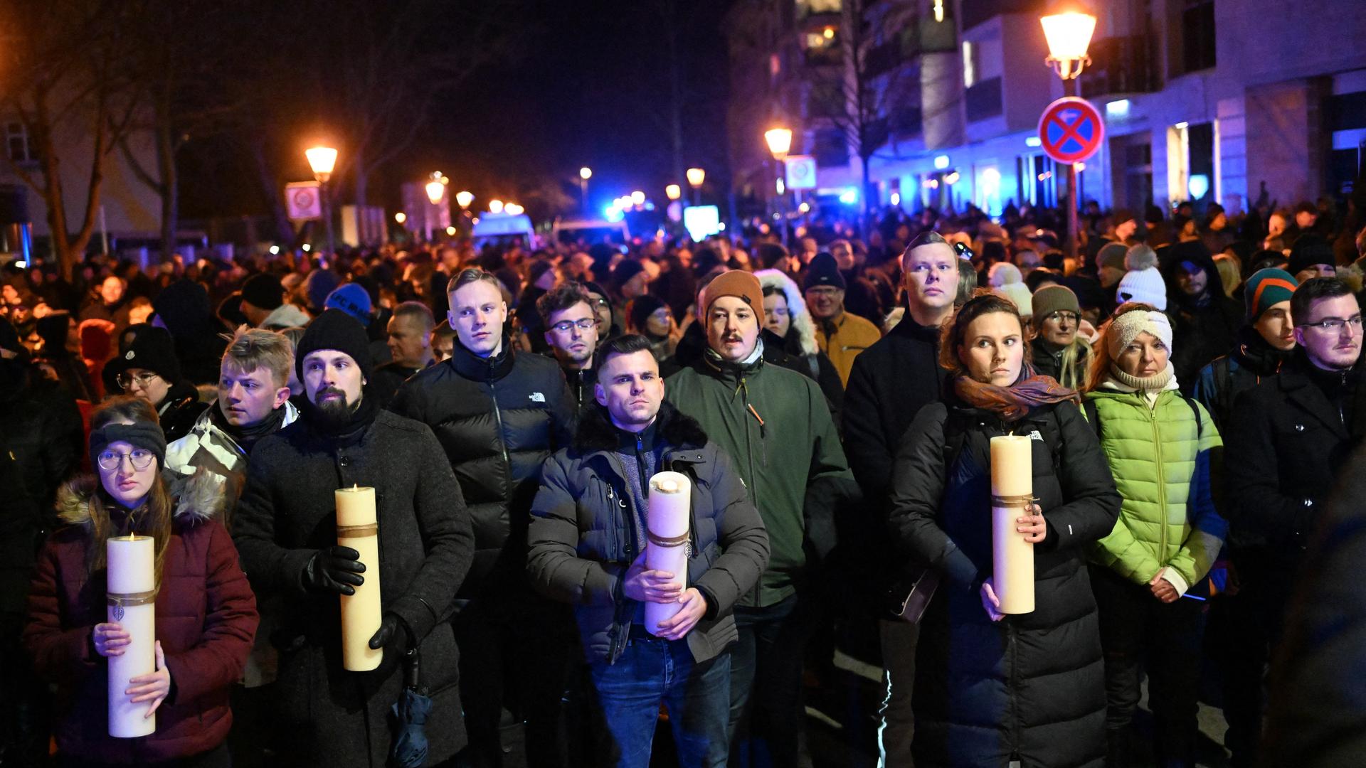 Mehrere hundert Menschen stehen auf der Straße. Die Personen im Vordergrund halten große Kerzen in den Händen.