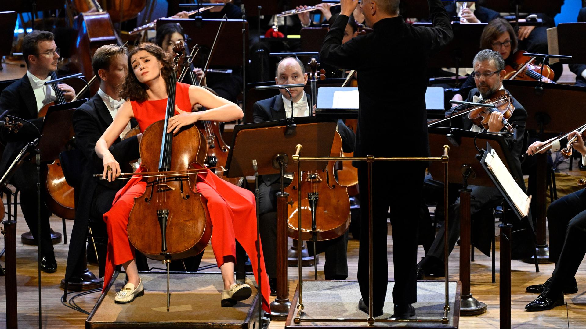 Die Cellist Anastasia Kobekina sitzt an ihrem Instrument auf der Bühne vor einem Orchester, rechts neben ihr der Dirigent Paavo Jarvi.