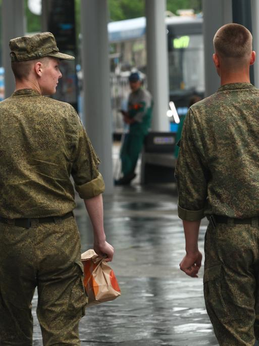 Zwei russische Soldaten schlendern über eine Straße in Moskau. Ansicht von hinten. 