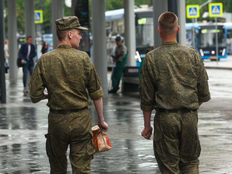 Zwei russische Soldaten schlendern über eine Straße in Moskau. Ansicht von hinten. 