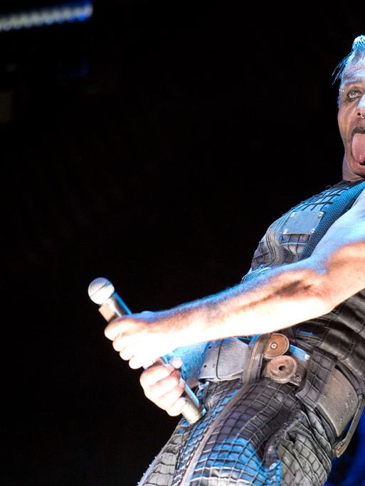 Der umstrittene Rammstein-Frontmann Till Lindemann steht geschminkt auf einer Bühne und macht mit dem Mikrofon eine Geste, die an einen Phallus erinnert. 