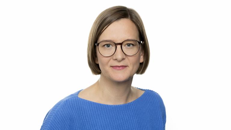 Portrait einer jungen Frau mit blauem Pullover und Brille vor weißem Hintergrund Portrait einer jungen Frau mit blauem Pullover und Brille vor weißem Hintergrund