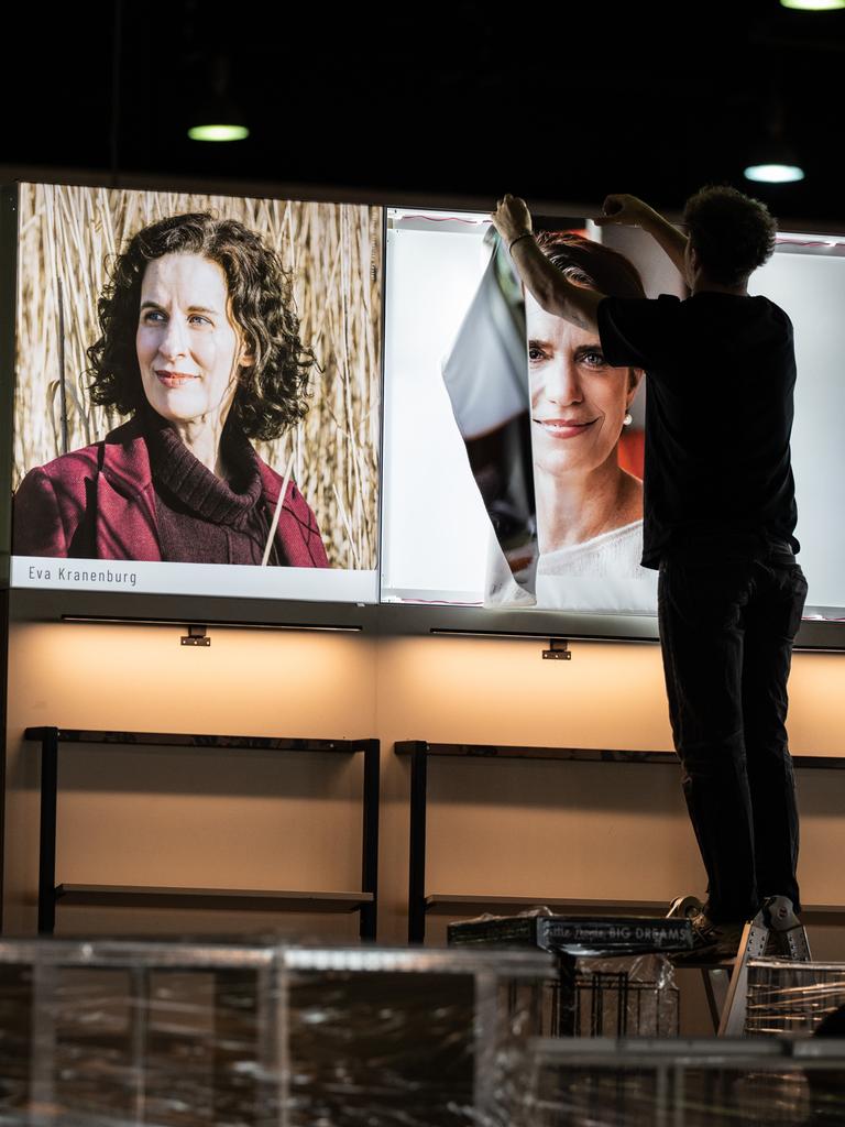Messebauer errichten den Stand eines Buchverlages auf der Buchmesse und hängen Fotos von Autorinnen und Autoren auf.