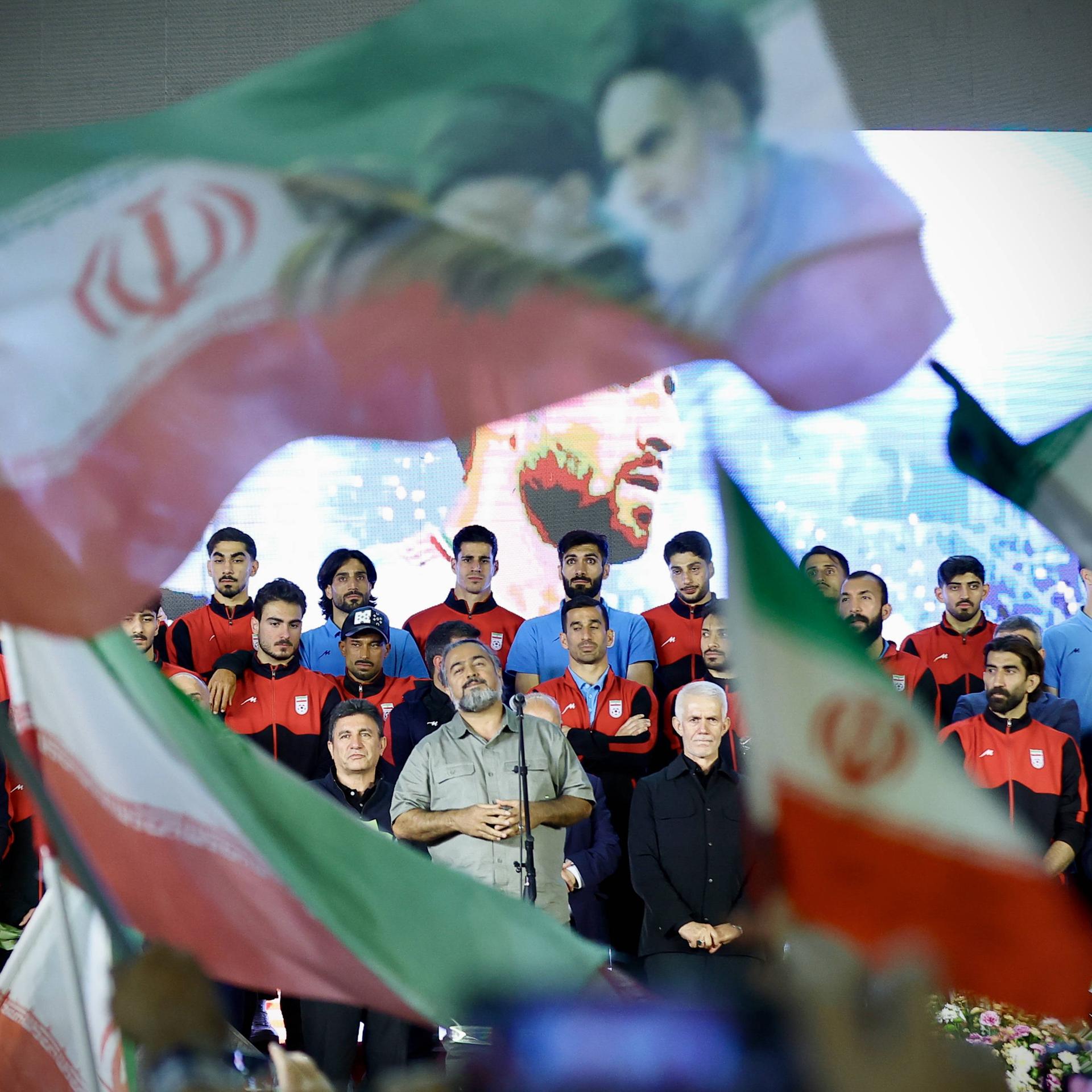 Veranstaltung der iranischen Fußballnationalmannschaft in Teheran vor der Weltmeisterschaft: Zu sehen sind Spieler, Cheftrainer und weitere Offizielle. Es werden Flaggen geschwungen. 