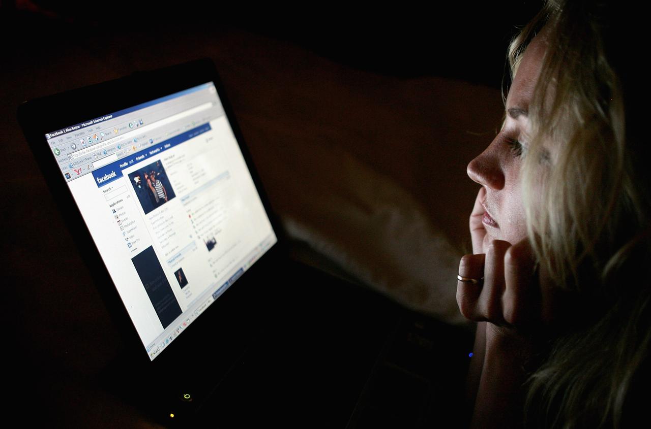 Eine Teenagerin schaut auf ihren Laptop, auf dem ihr Facebook-Profil angezeigt wird.
