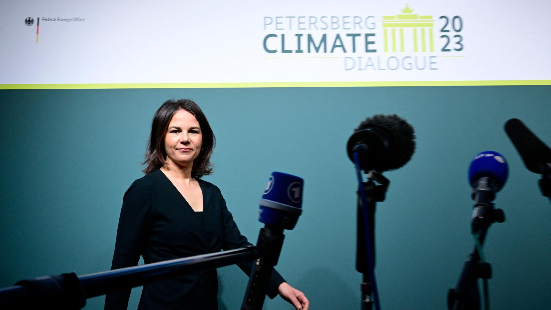 Bundesaußenministerin Baerbock geht beim Petersberger Klimadialog auf der Bühne auf Mikrofone zu.