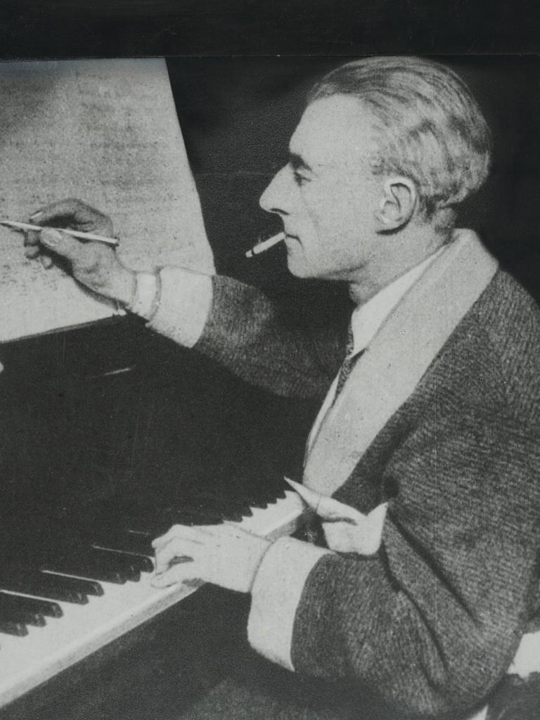 Der Komponist Maurice Ravel sitzt auf einem undatierten Foto am Klavier und hält einen Stift in der rechten Hand, mit dem er auf einem Notenblatt schreibt. 