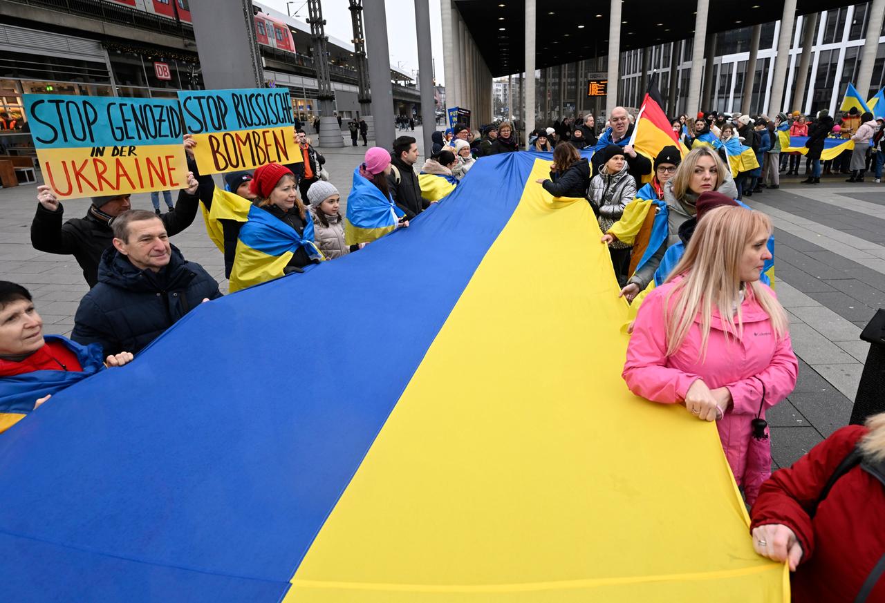 Demonstrierende in Köln halten am Bahnhof eine grosse Fahne der Ukraine fest.