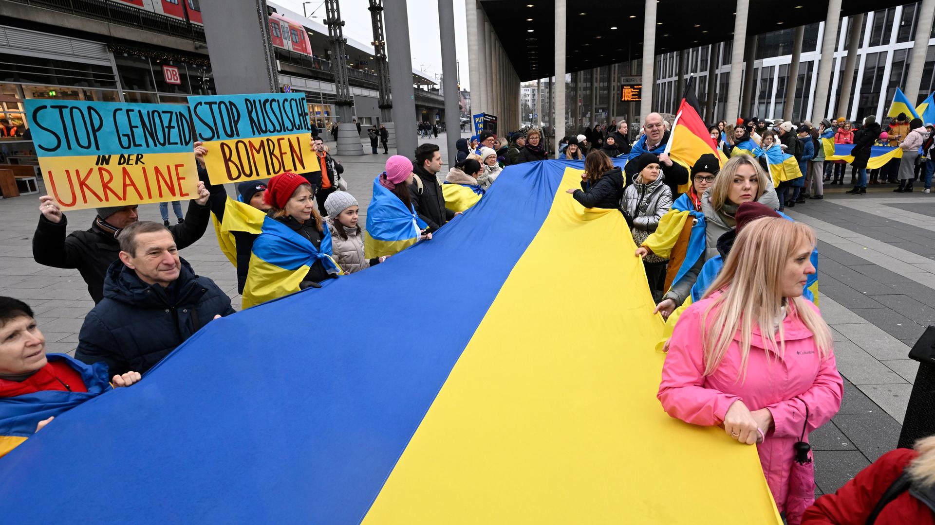 Demonstrierende in Köln halten am Bahnhof eine grosse Fahne der Ukraine fest. Demonstrierende in Köln halten am Bahnhof eine grosse Fahne der Ukraine fest.