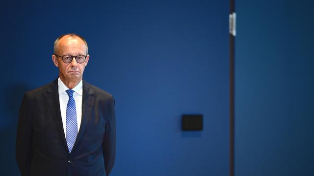 Auf dem Bild ist Friedrich Merz von der Partei CDU zu sehen. Er steht vor einer blauen Wand.