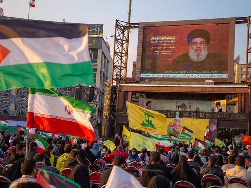 Flaggenschwenkende Menge vor einer Leinwand bei einer Übertragung der Rede des Hisbollah-Generalsekretärs Hassan Nasrallah.