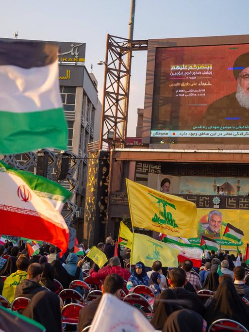 Flaggenschwenkende Menge vor einer Leinwand bei einer Übertragung der Rede des Hisbollah-Generalsekretärs Hassan Nasrallah.