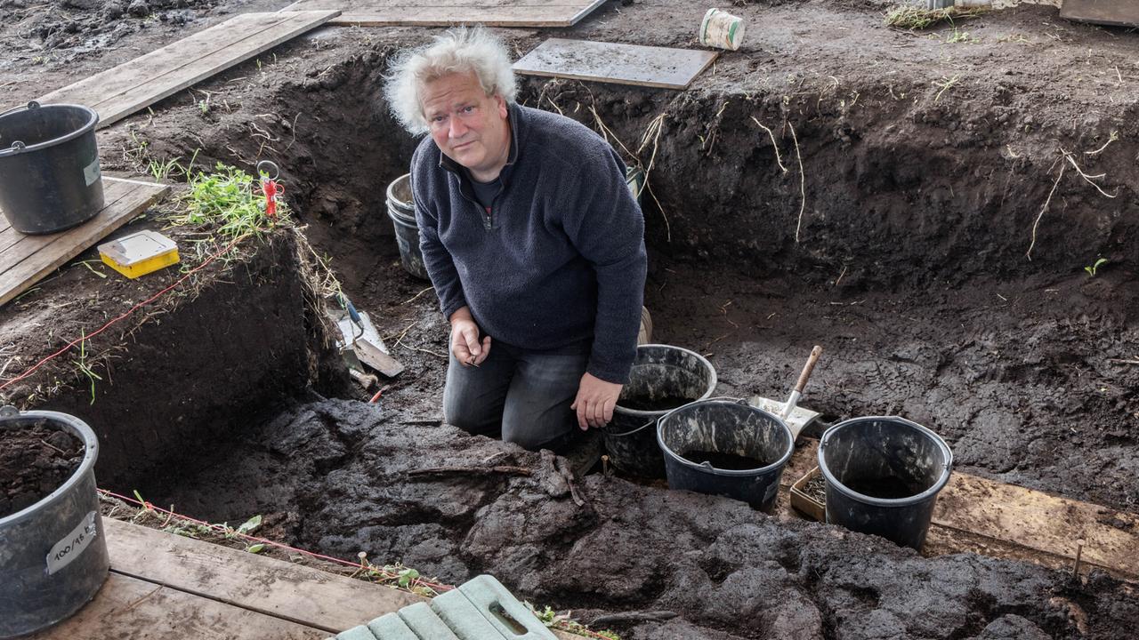 Ein Mann steht an einer archäologischen Grabungsstelle und schaut in die Kamera.