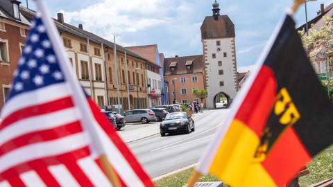 Die Fahnen der USA und Deutschlands, im Hintergrund ein Marktplatz mit Kirche.