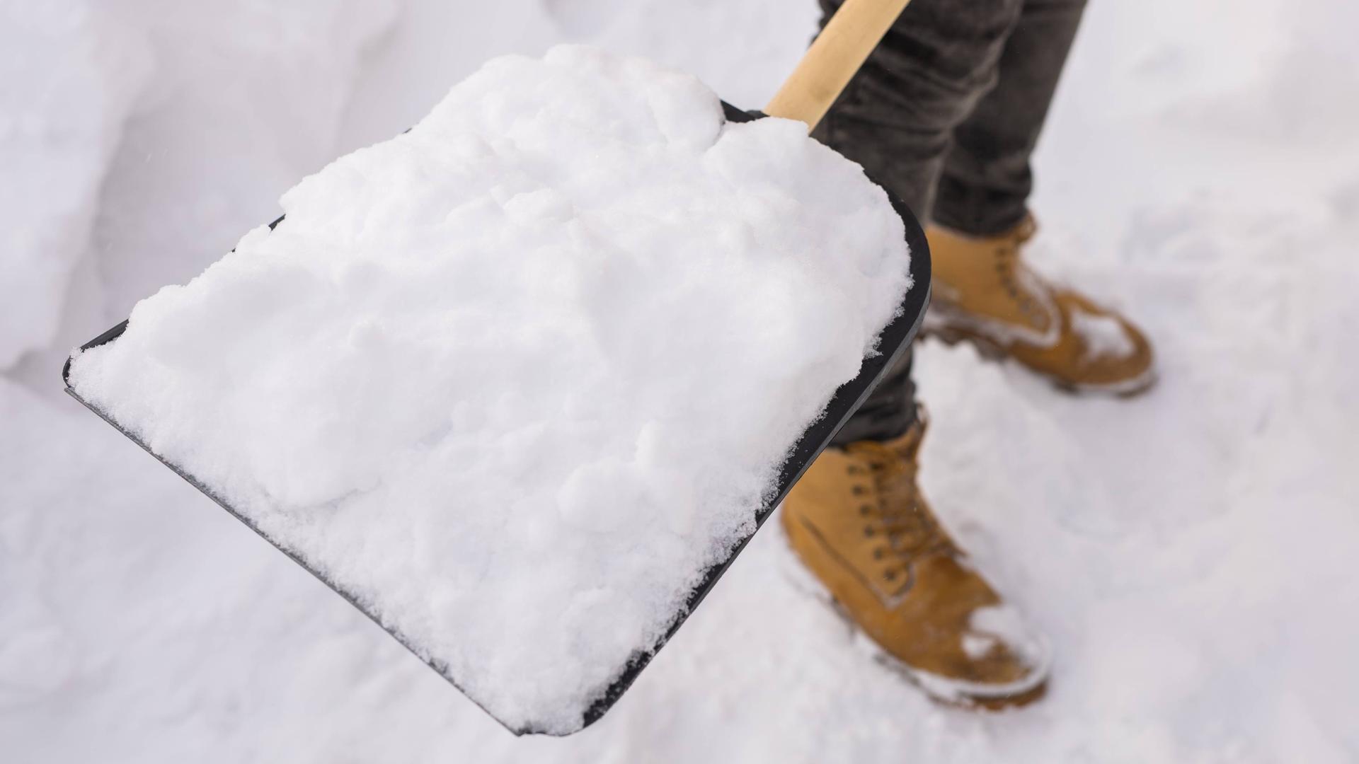 Nahaufnahme einer Person, die Schnee schaufelt.